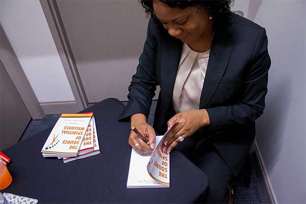 Tinasha at a book signing, signing one of her books from the Source of Wellness series.
